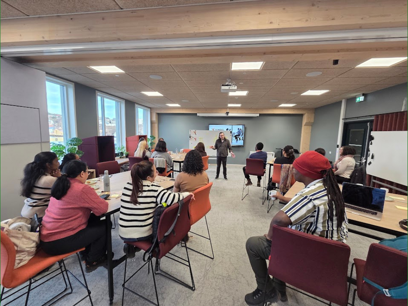 Mange mennesker sitter i et rom med rggen til og ser mot en person som snakker i forgrunnen