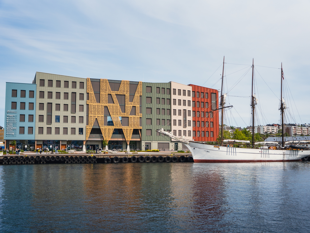 Campus Cristiansund med en hvit seilbåt foran. i forgrunnen ser vi vann som er havnebassenget i Kristiansund