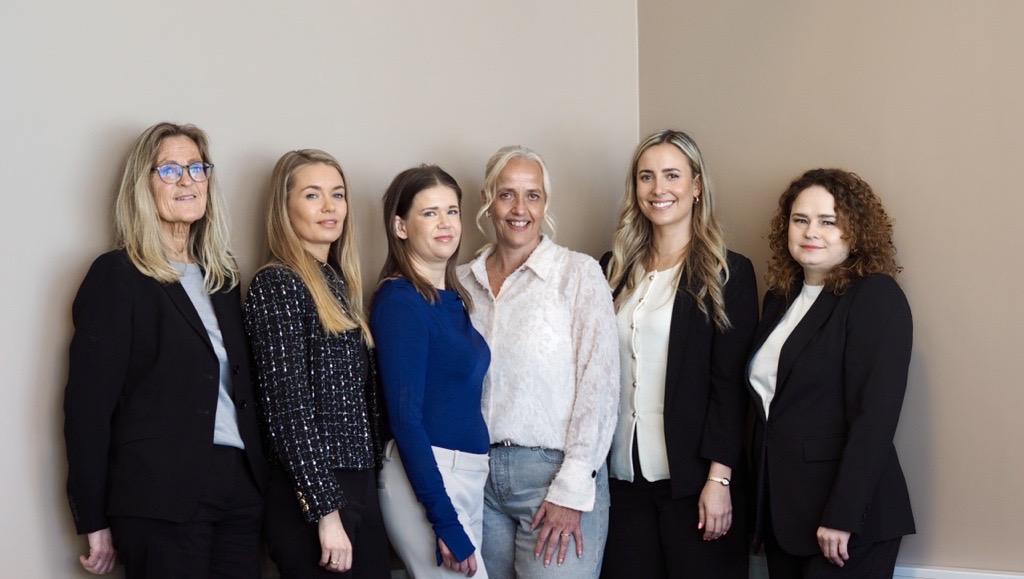 Mange kvinner står mot en vegg og smiler mot kampera